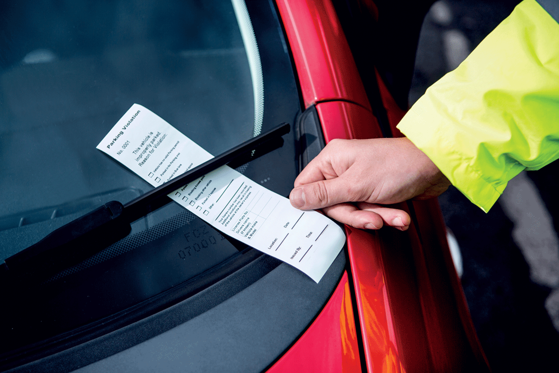 Parking notice being placed under windscreen wiper on red car