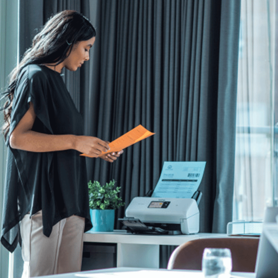 Female stood holding document next to ADS-4500W, caninet, glass, plant