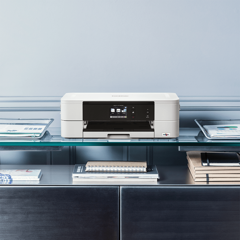 White inkjet printer on glass desk surrounded by files - DCPJ774DW