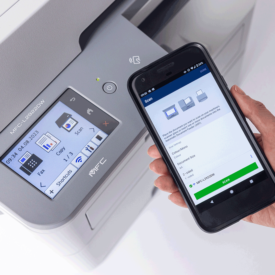 <p>Person holding mobile phone next to Brother MFCL2922DW printer</p>