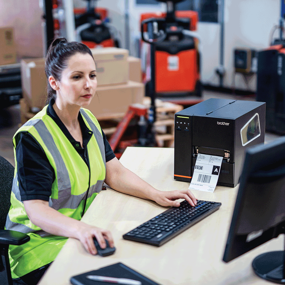 A female warehouse worker printing a label from a desktop computer to a Brother industrial label printer