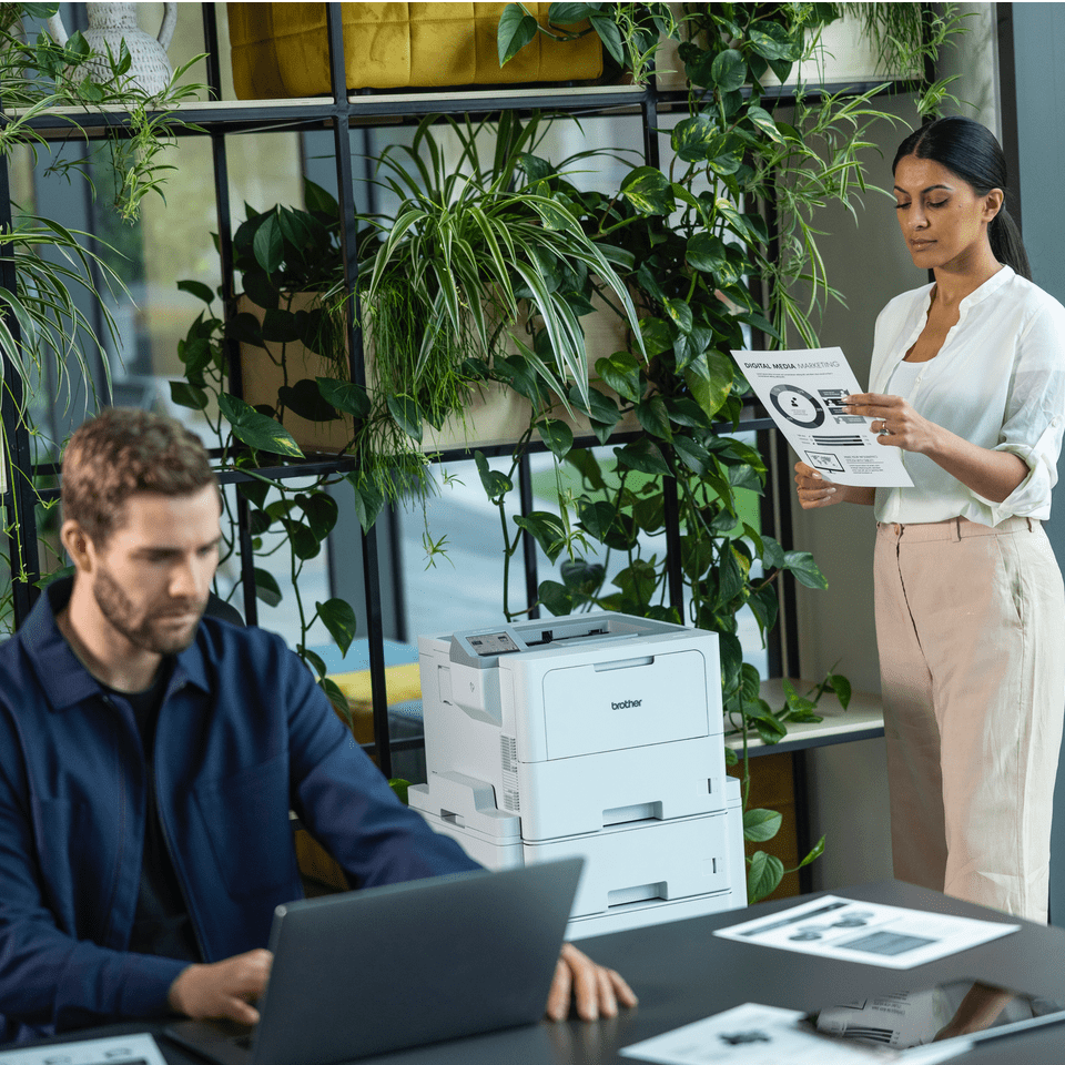 Female stood at Brother HL-L6410DN with a male colleague working at a desk next to her