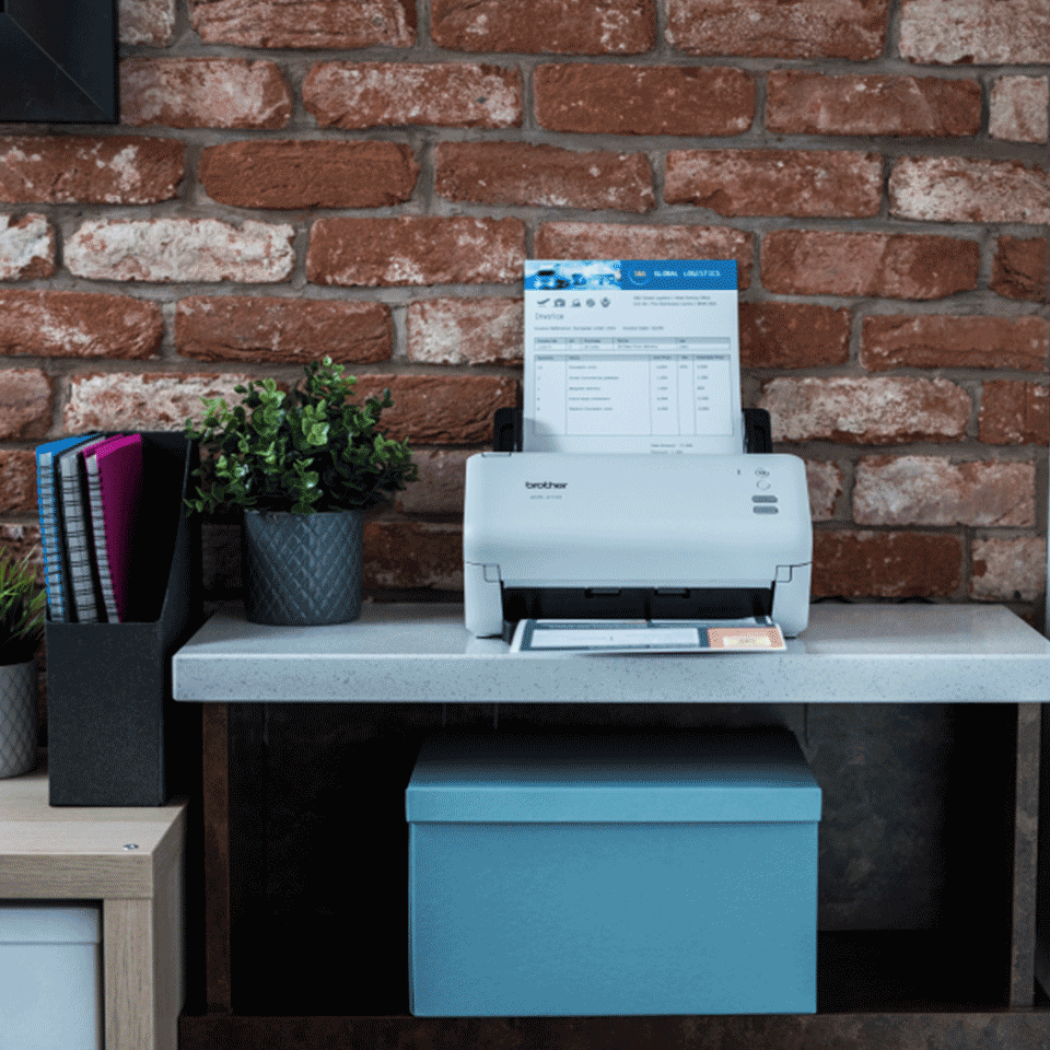 ADS-4100 on desk against brick wall, plant, folders, boxes