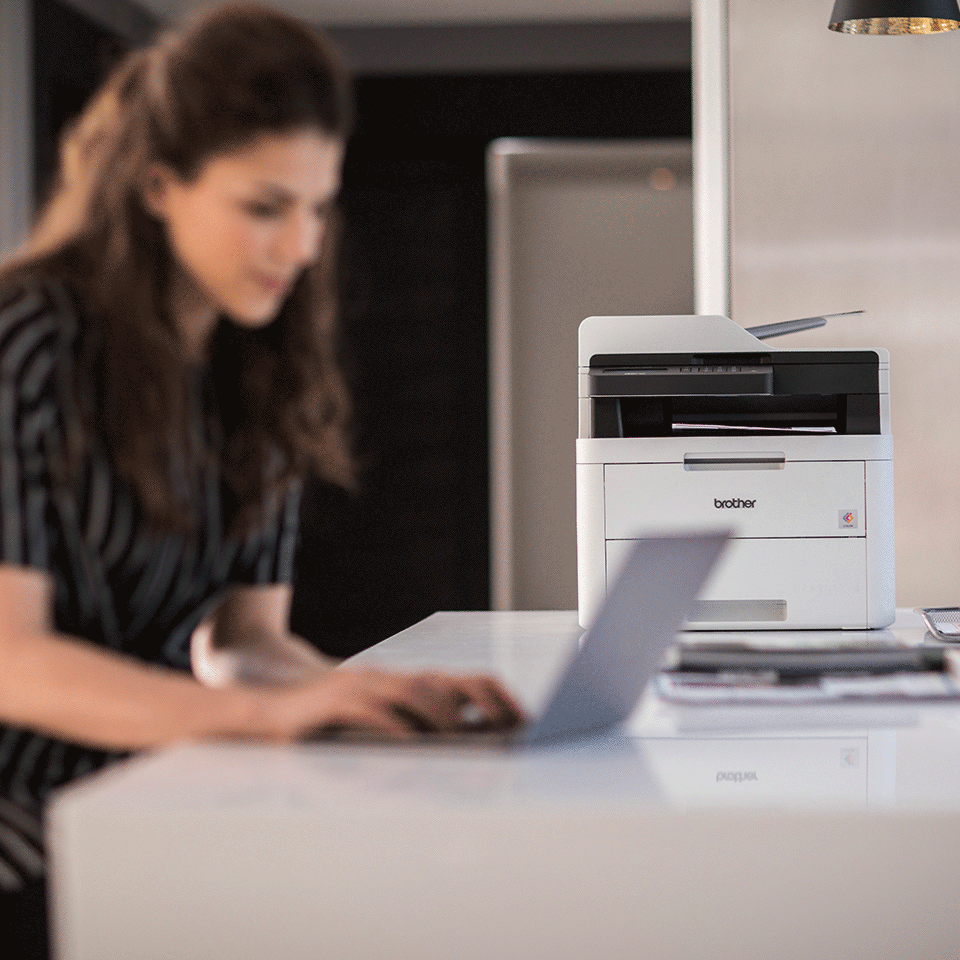 Woman using laptop with MFCL3730CDN colour printer in house