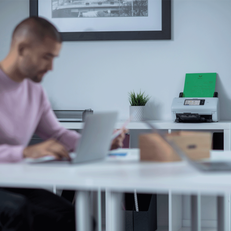Man sat at desk, ADS-4700W, laptop, plants, documents