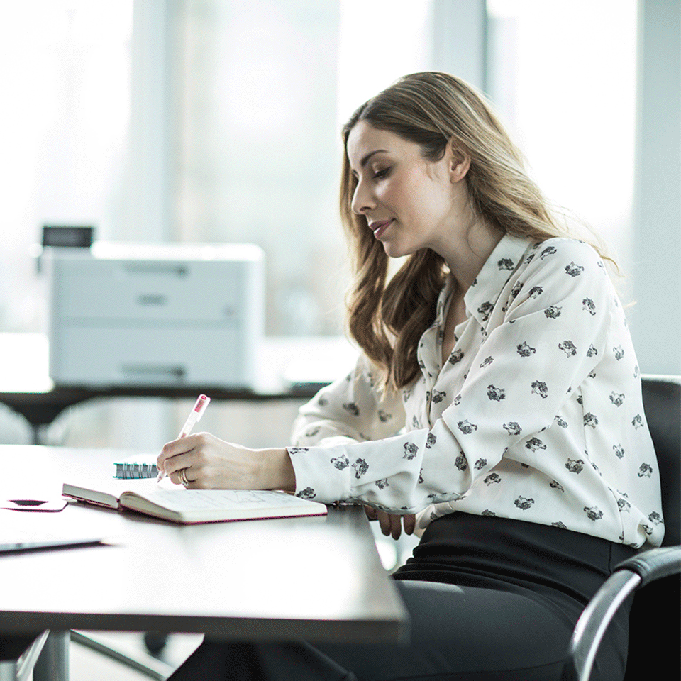 Woman sat at desk with HLL3270CDW colour printer in background