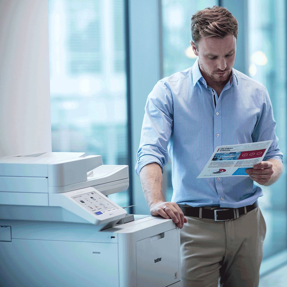 Man wearing blue shirt stood next to printer holding colour document