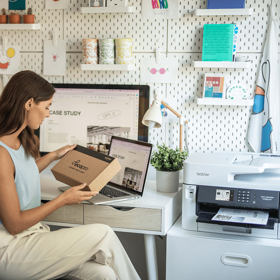 Woman holding a cardboard EcoPro box, sat next to the MFC-J5340DWE