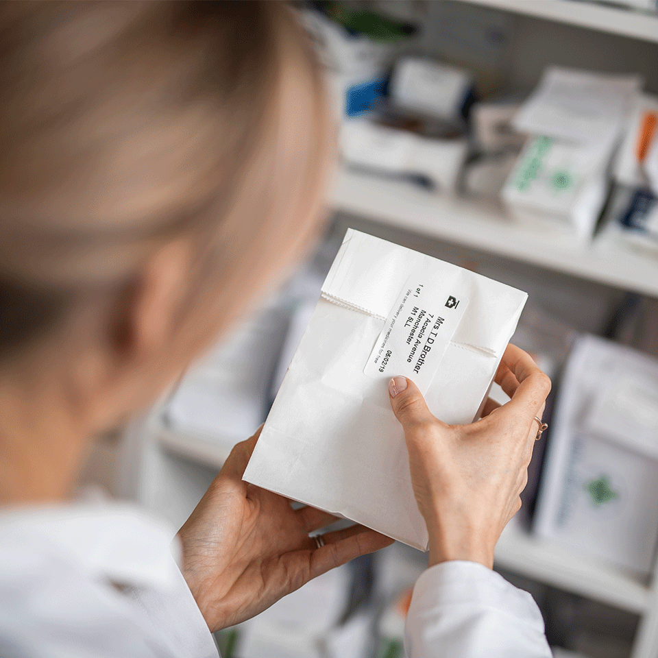 Pharmacist in pharmacy putting label on prescription