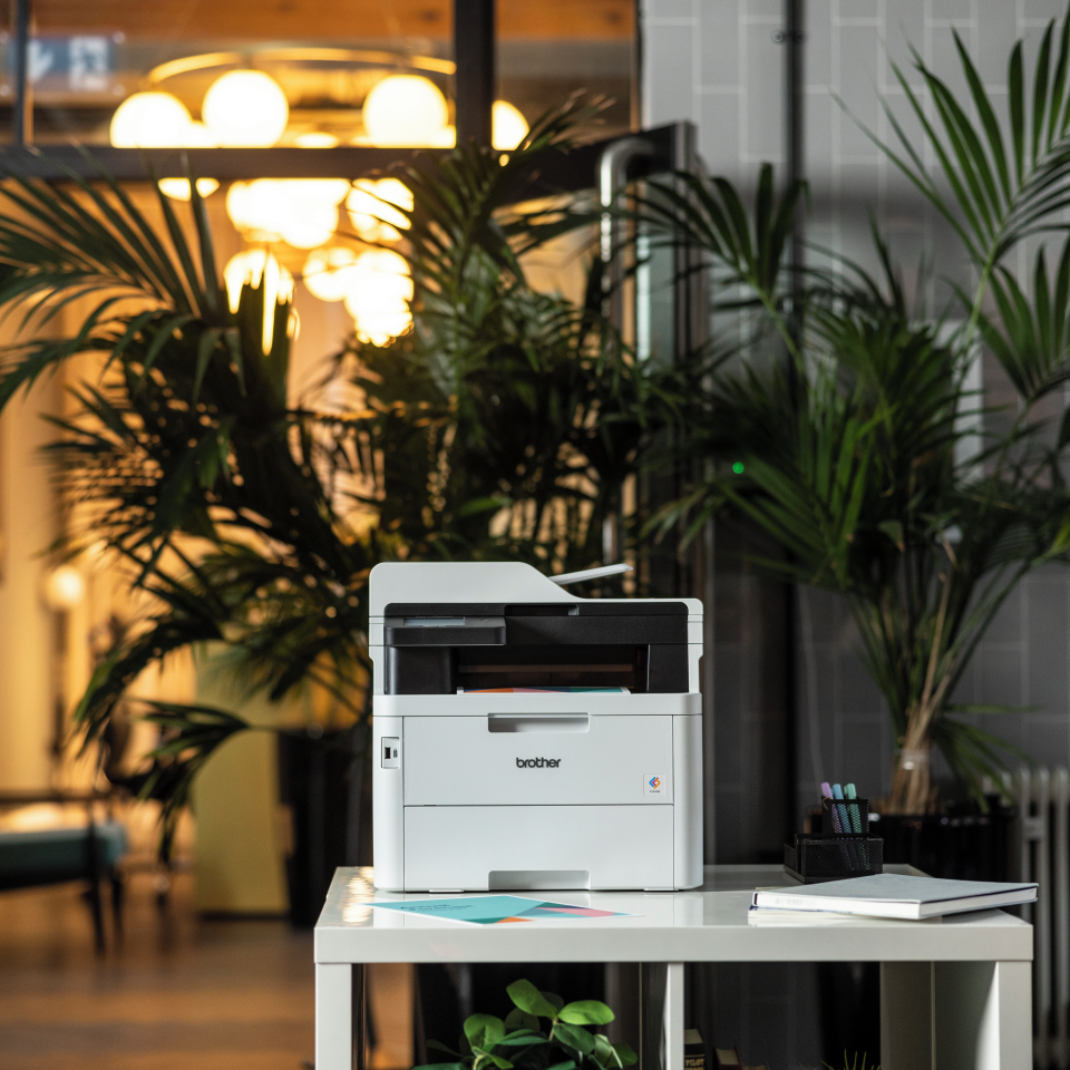 MFC-L3760CDW LED printer front facing in a modern office setting surrounded by full colour outputs