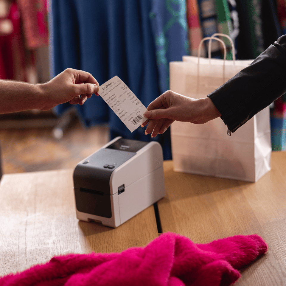 <p>Brother TD-2310D203 on a wooden counter top in a clothing retail store, being used to print a receipt</p>