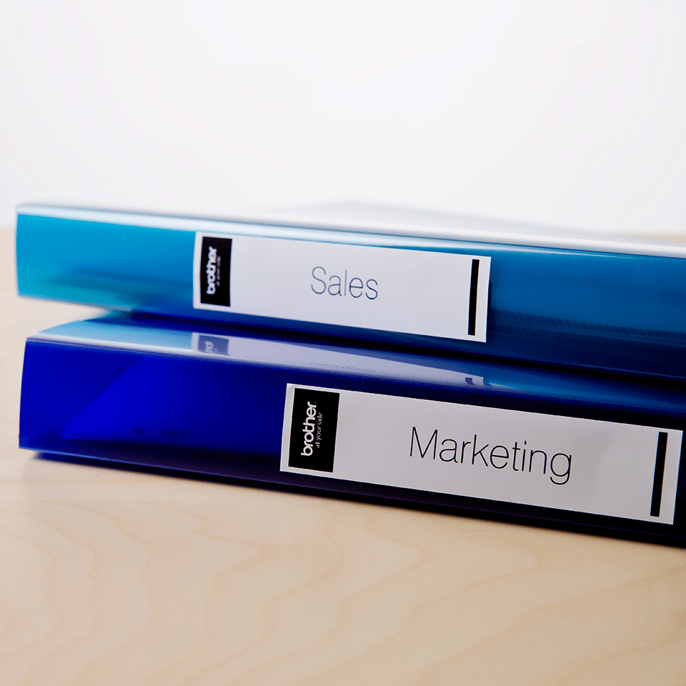 File folders on a desk with a Brother black on white DK label on the spine of the folder