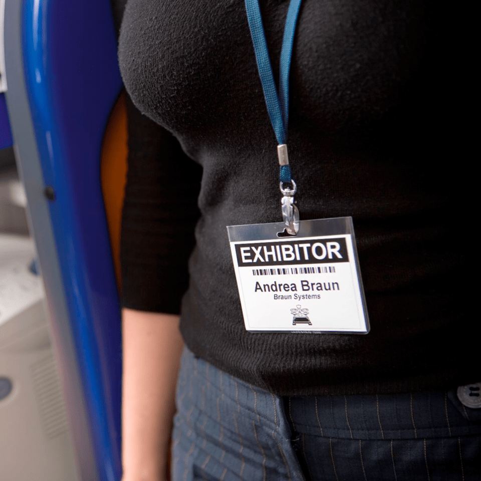 A woman wears a lanyard around her neck with an event pass printed on the Brother QL-820NWBVM that says "Exhibitor"