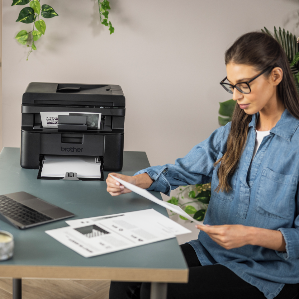 <p>Woman reviewing output next to the mono laser DCPL1660W printer</p>