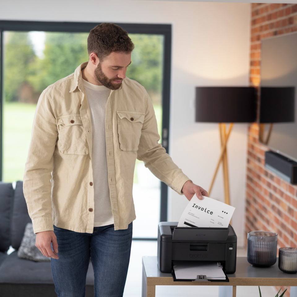 <p>Man removing output from the HL-L1242W mono laser printer</p>