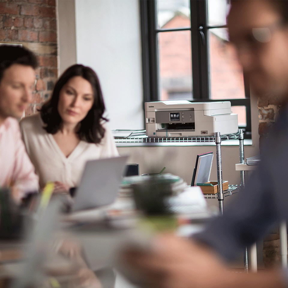 Group of colleagues working with DCP-J1100DW printer in the background