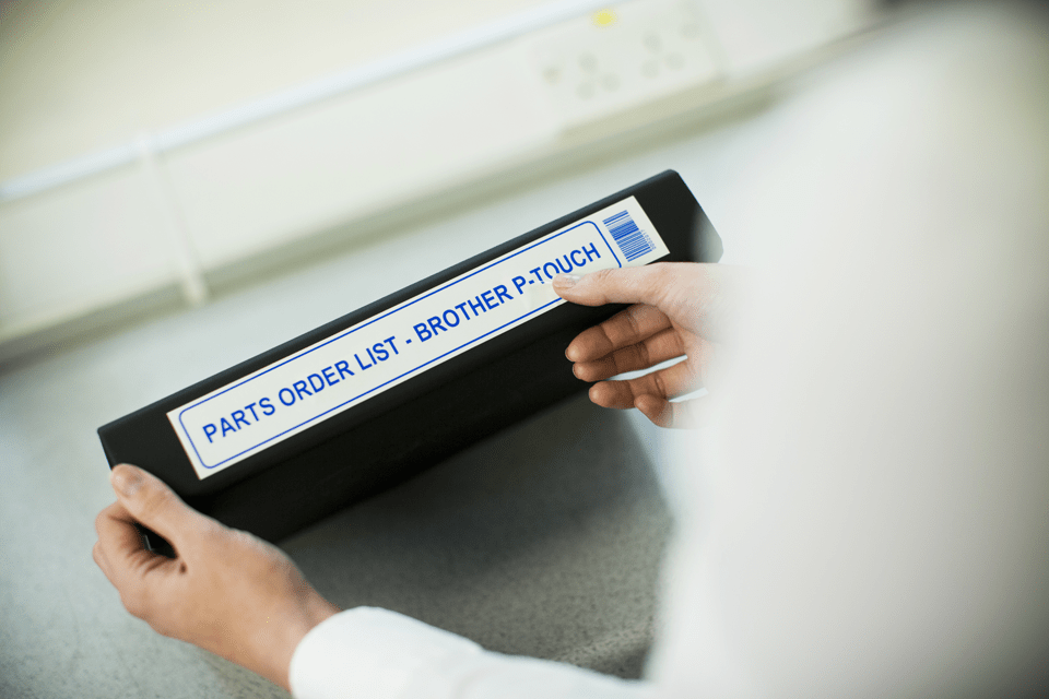 Brother TZe-263 label tape cassette - blue on white - a woman attaches a label to the side of a document archive box.