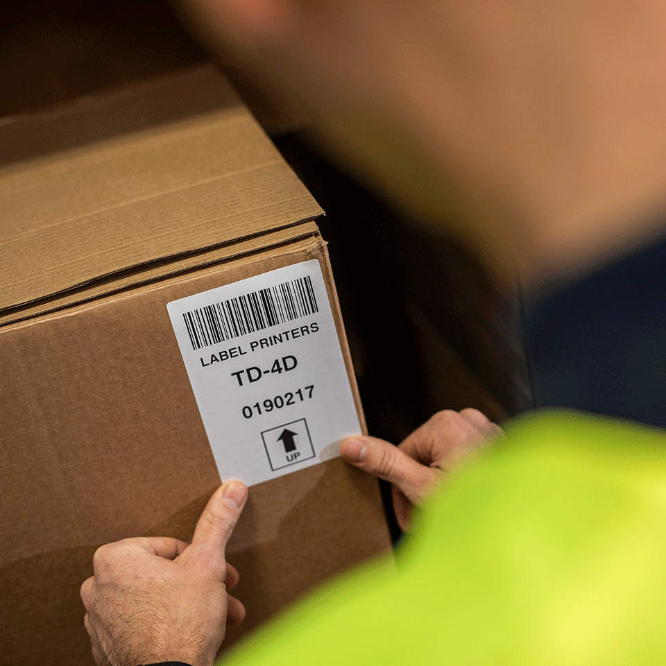 Man wearing hi-vis in warehouse applying shipping label to brown box