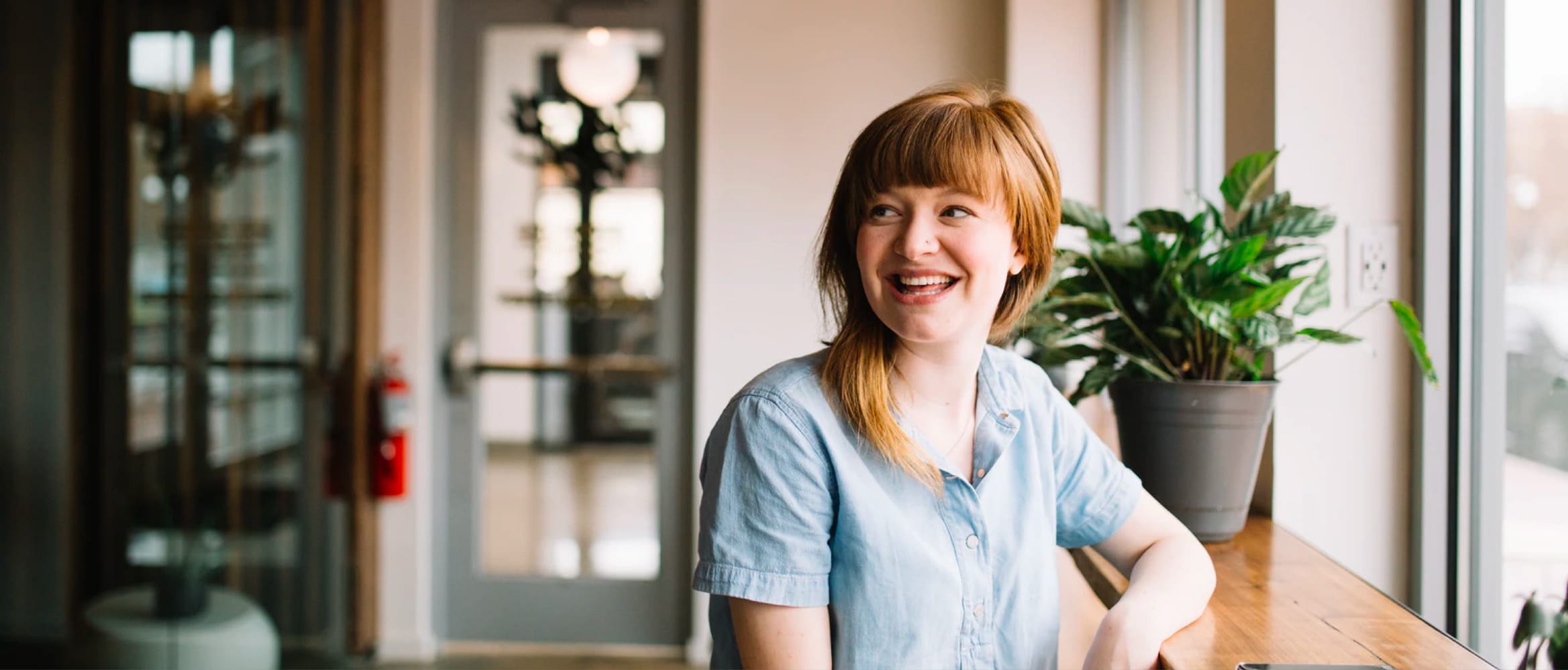 A lady smiling at something out of view while sitting at a countertop next to a window in a SOHO environment