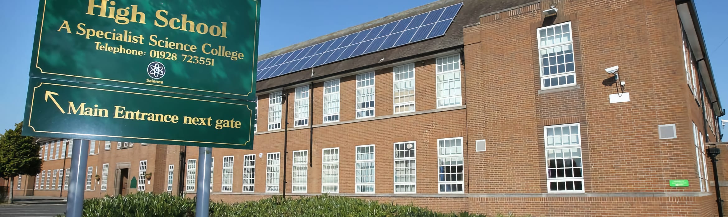 Helsby High School building with a green sign showing information in the foreground