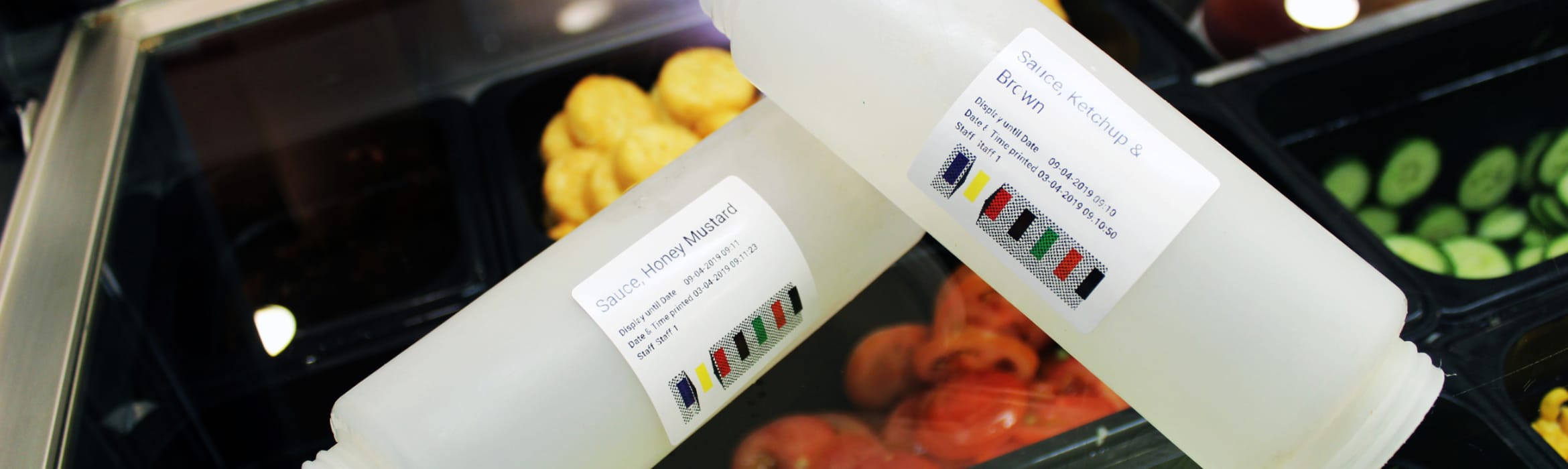 Two empty sauce containers, one labelled Honey Mustard and the other Ketchup and Brown, with salad trays in the background