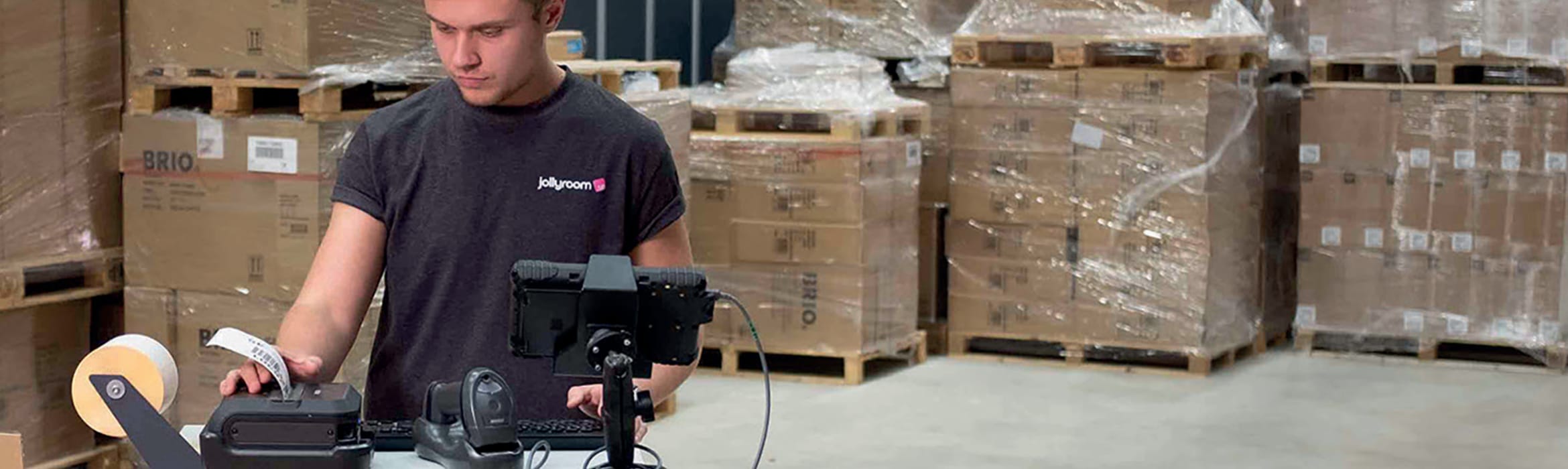 A male warehouse worker printing barcode labels with pallets of brown cardboard boxes in the background