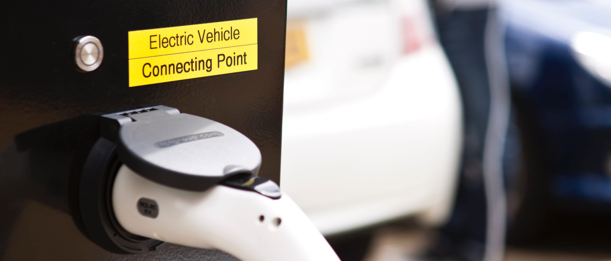 Close-up of an electric vehicle connecting point with vehicle and owner in the background