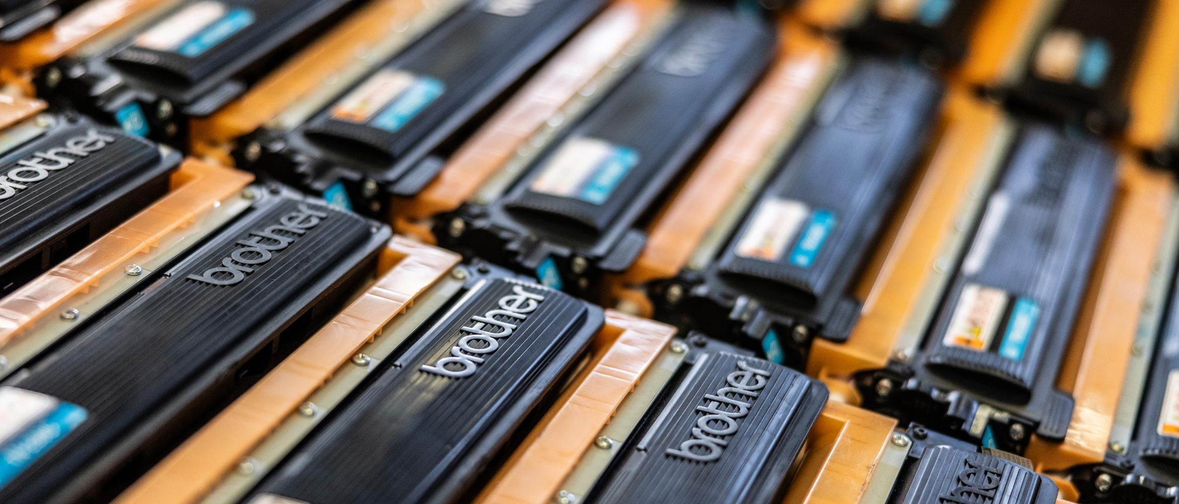 3 rows of orange and black Brother toner cartridges lay side by side