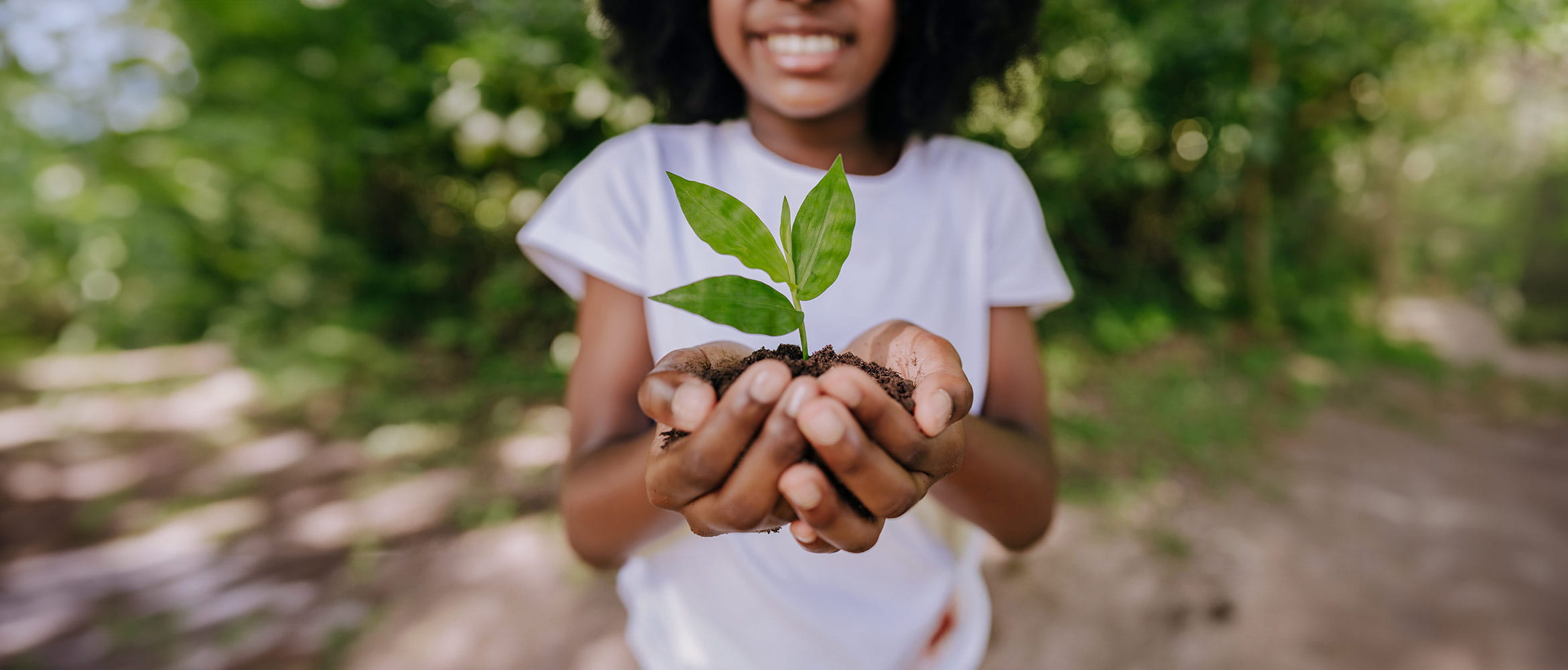 Girl in white tshirt holding a tree shoot in her cupped hands