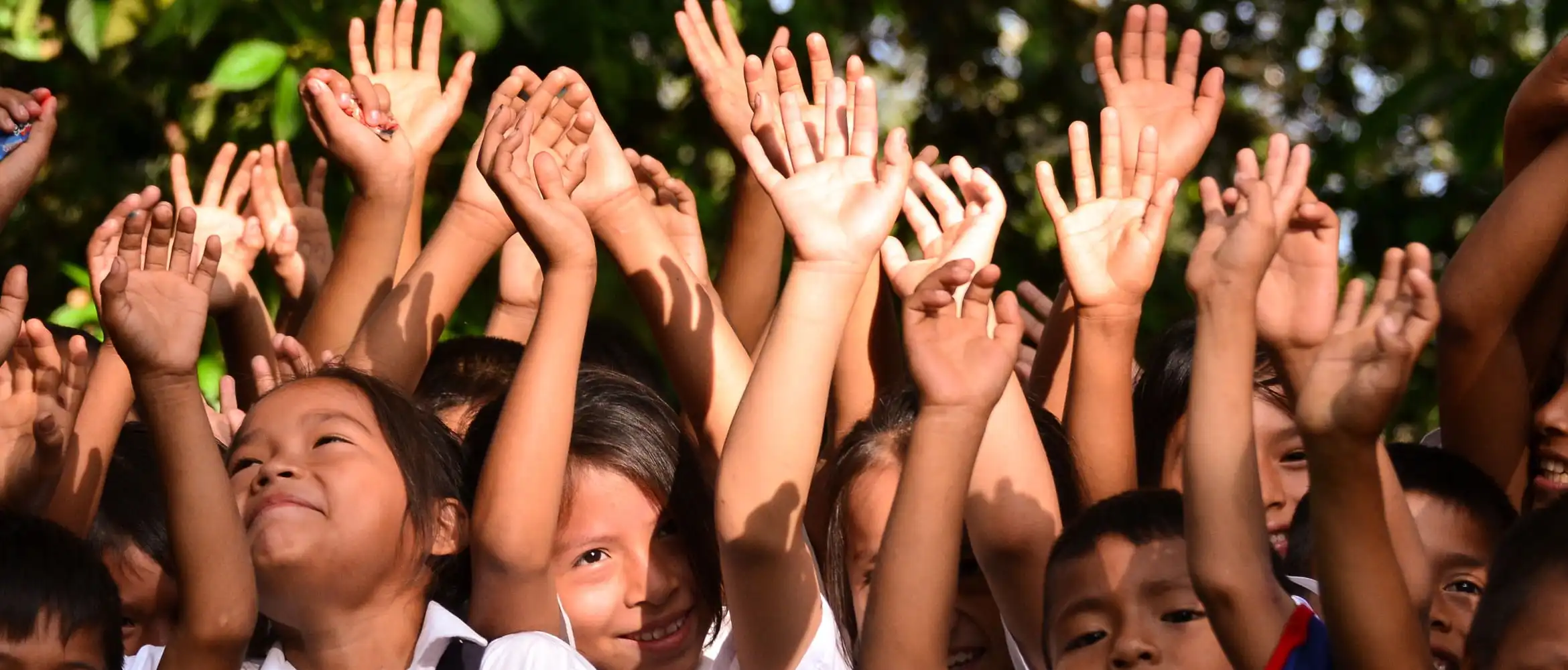 Group of schoolchildren smiling with their hands in the air