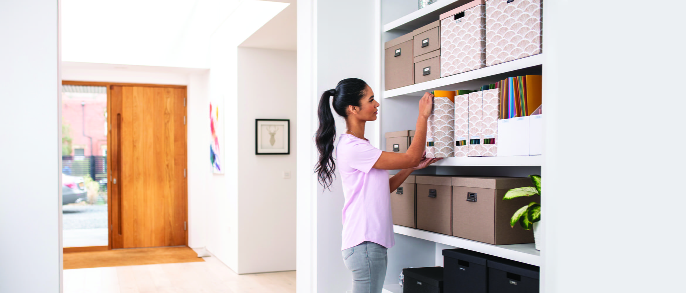 Femme debout dans sa maison avec une porte en arrière-plan, organisant des dossiers et des boîtes sur des étagères.