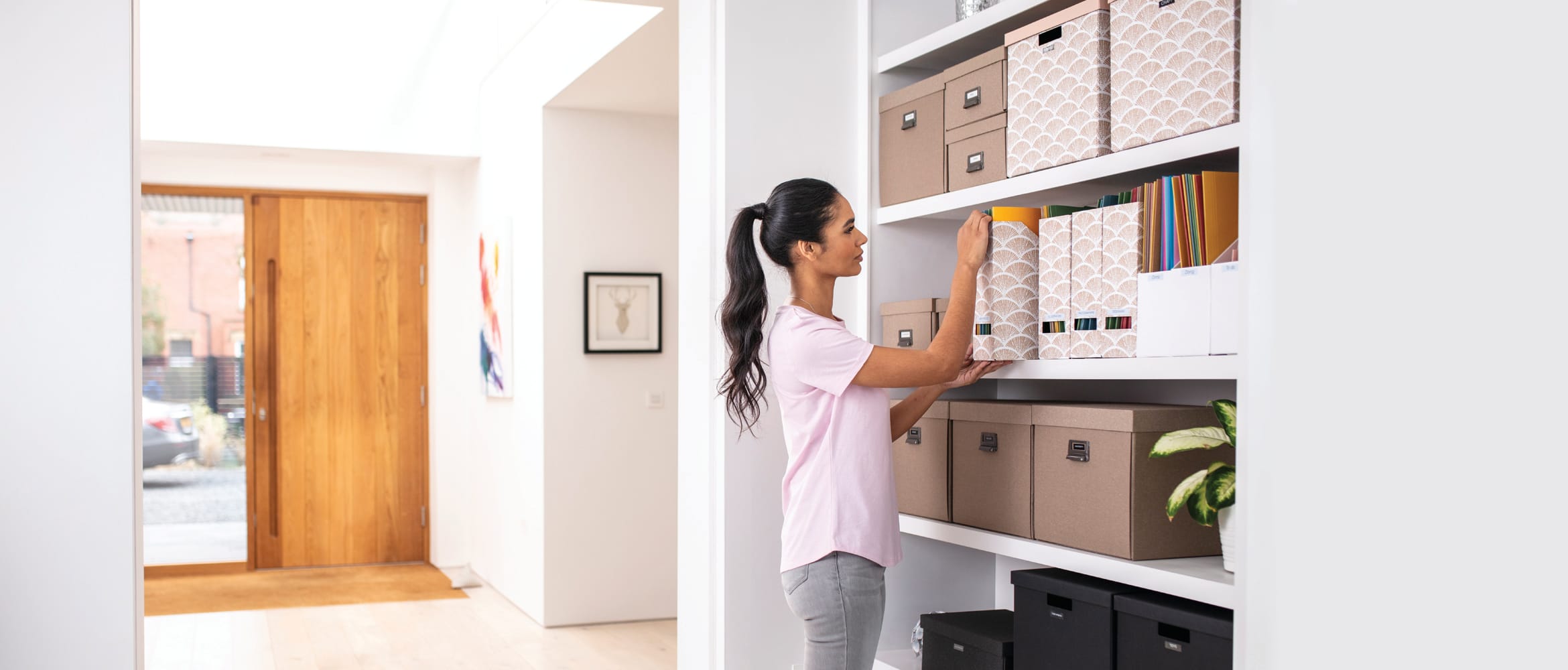 A lady pulling a labelled box file from a bookshelf in a home office environment