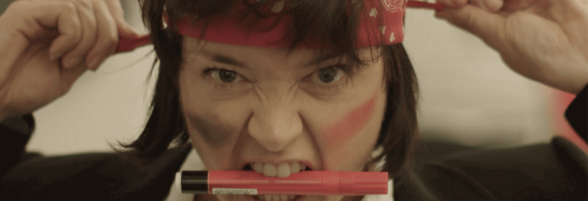 Woman snarling while gripping pen in teeth and tying headband to illustrate an office dispute caused by stolen items