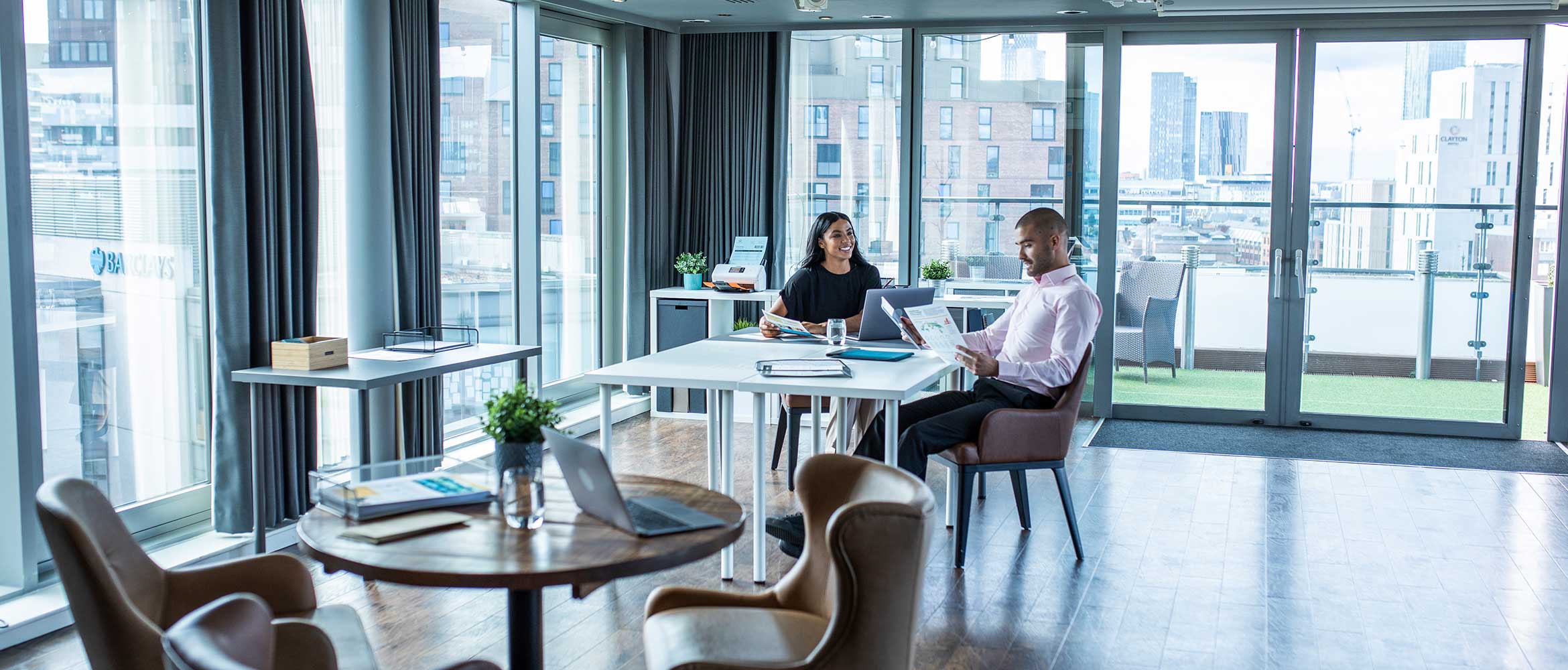 Male and female sat at desk in office, desk, chairs, stationary , scanner, buildings