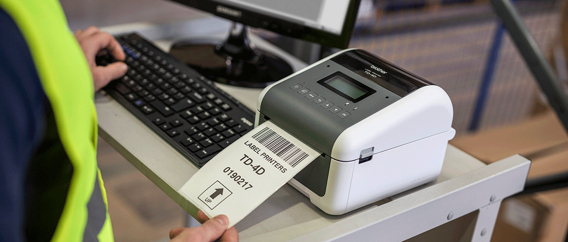 Man taking label from Brother TD-4D label printer on desk with computer monitor and keyboard