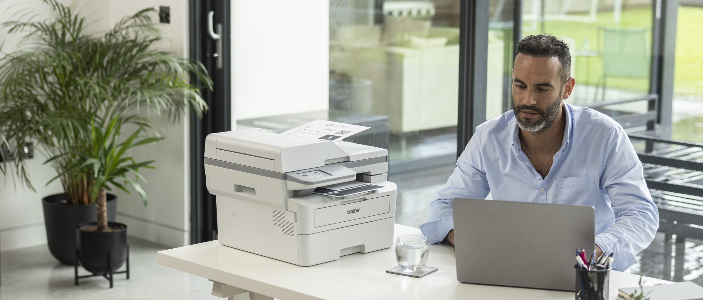 Man in the office working on laptop with Brother printer on the desk