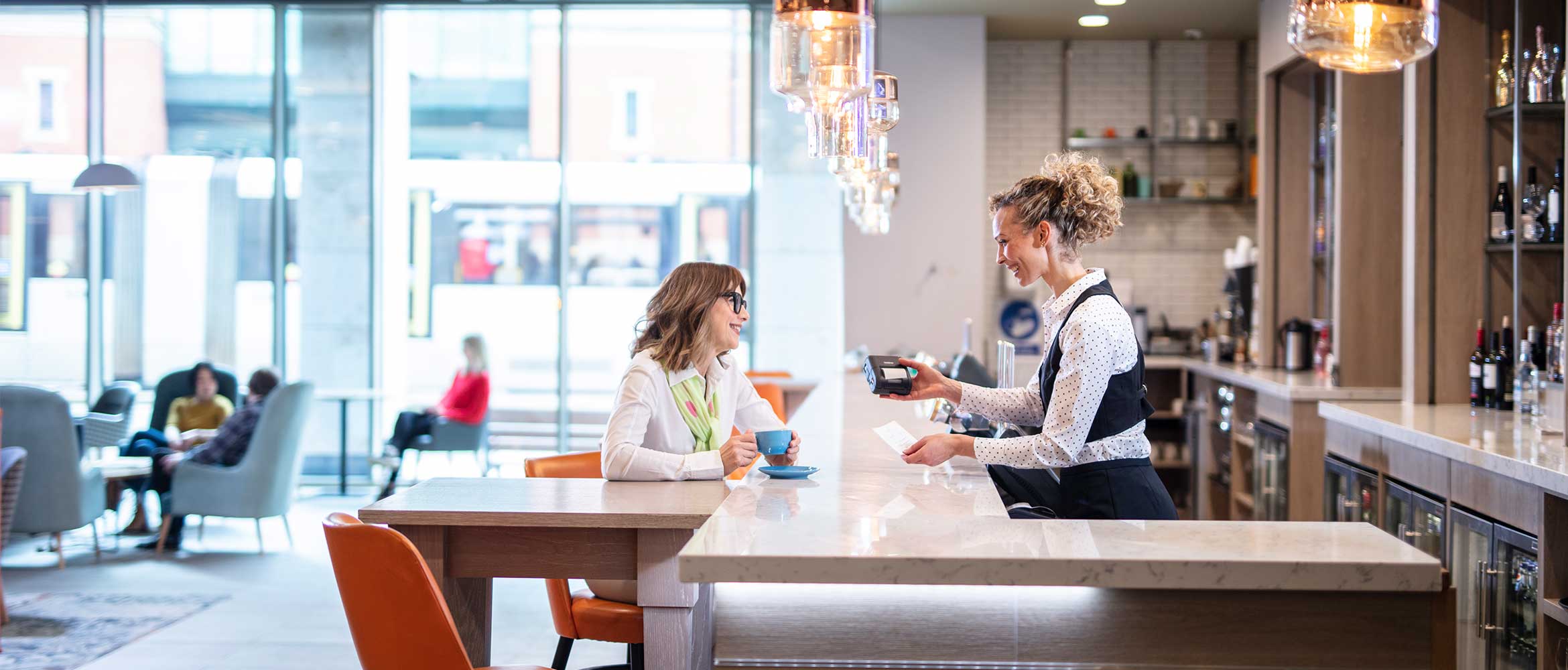 Barmen sert une femme assise sur un tabouret de bar, bouteilles, lampes, chaises, tasses