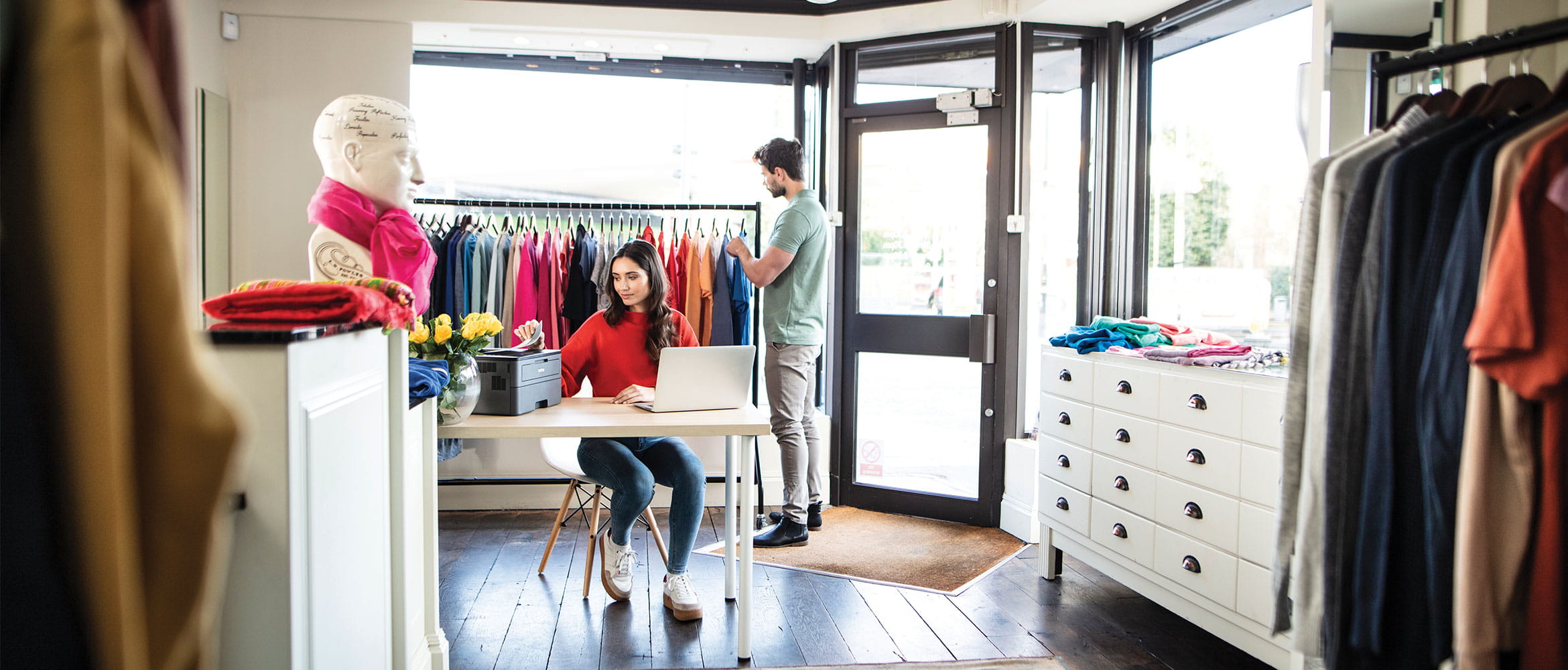 Man shopping for clothes and woman sat at desk printing document in a retail clothes store