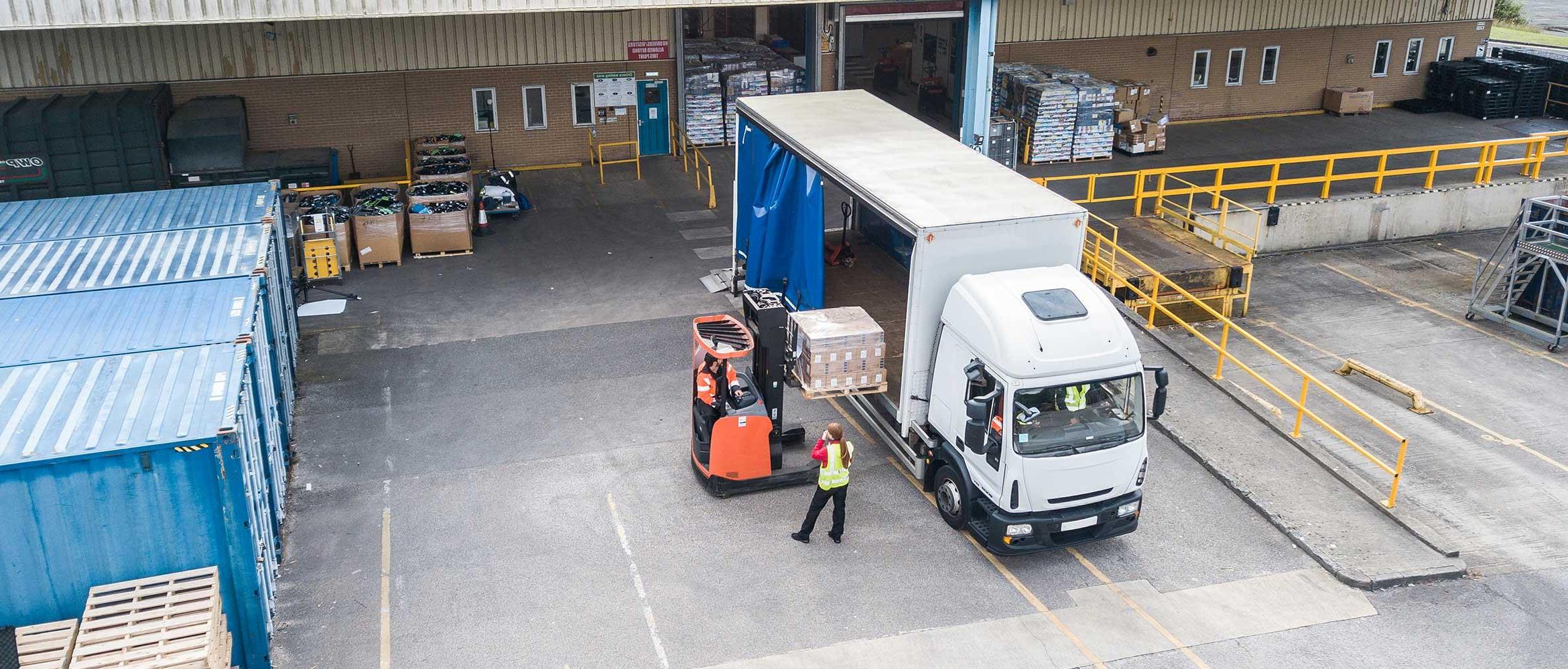 Transportation and logistics, aerial view of loading bay, white and blue van, orange fork lift, person wearing hi-vis