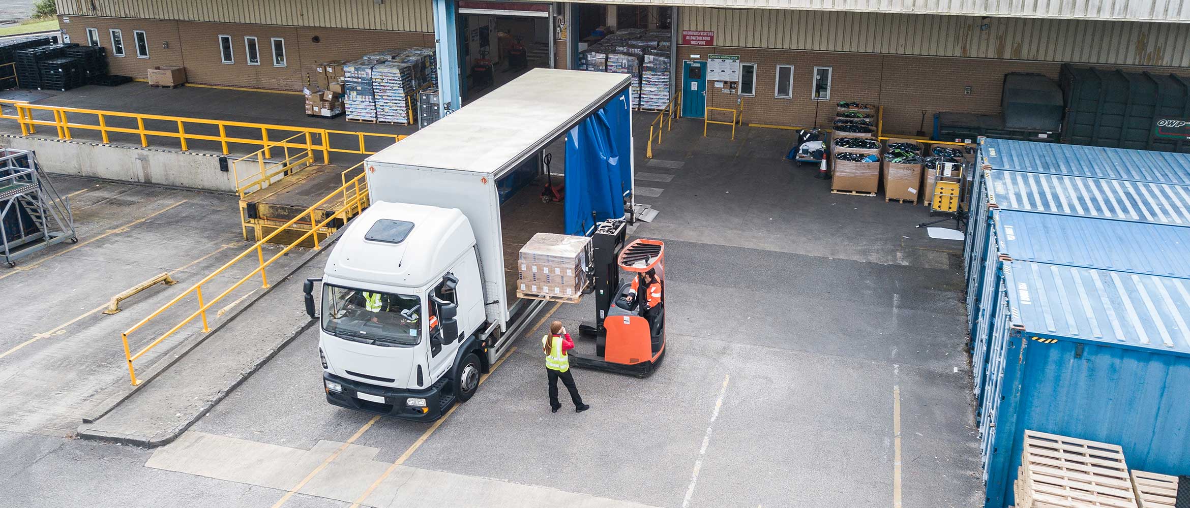 Transportation and logistics, aerial view of loading bay, white and blue van, orange fork lift, person wearing hi-vis