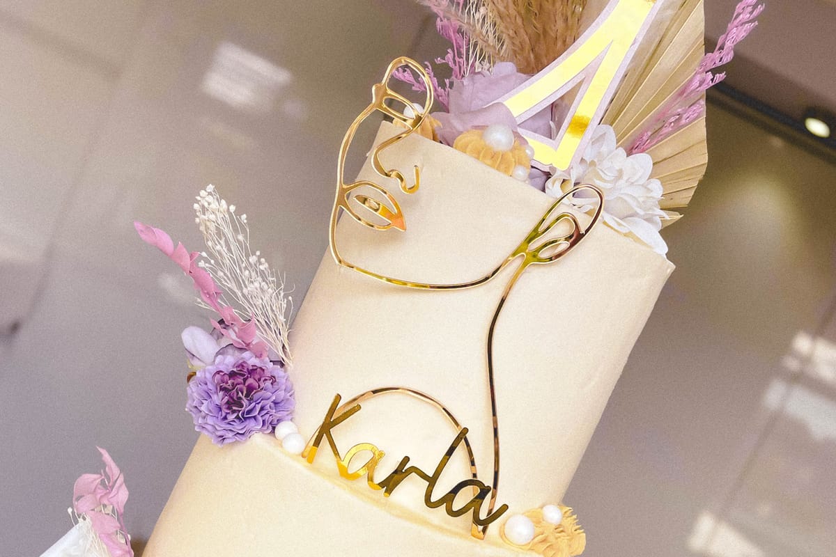 Close-up of a tiered cake, covered in smooth cream icing with gold, purple and white decorations