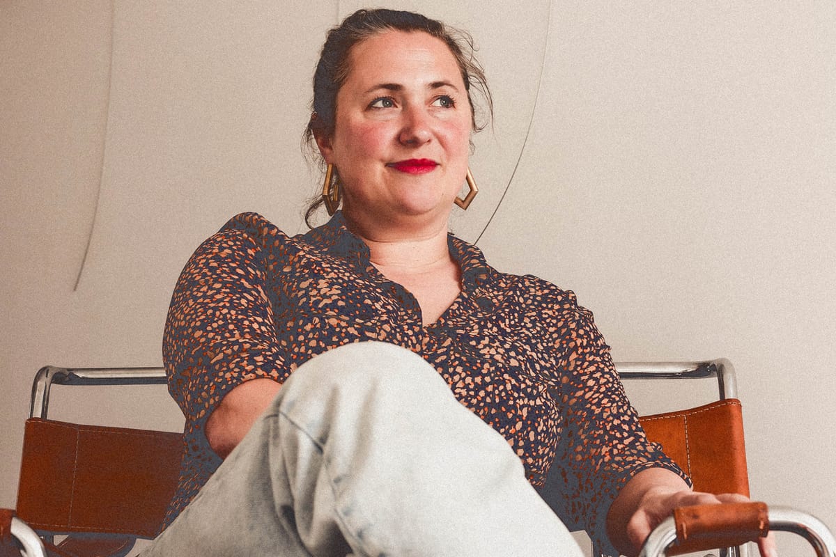 Andrea Ainsworth smiling while sat on a chair in front of a white wall