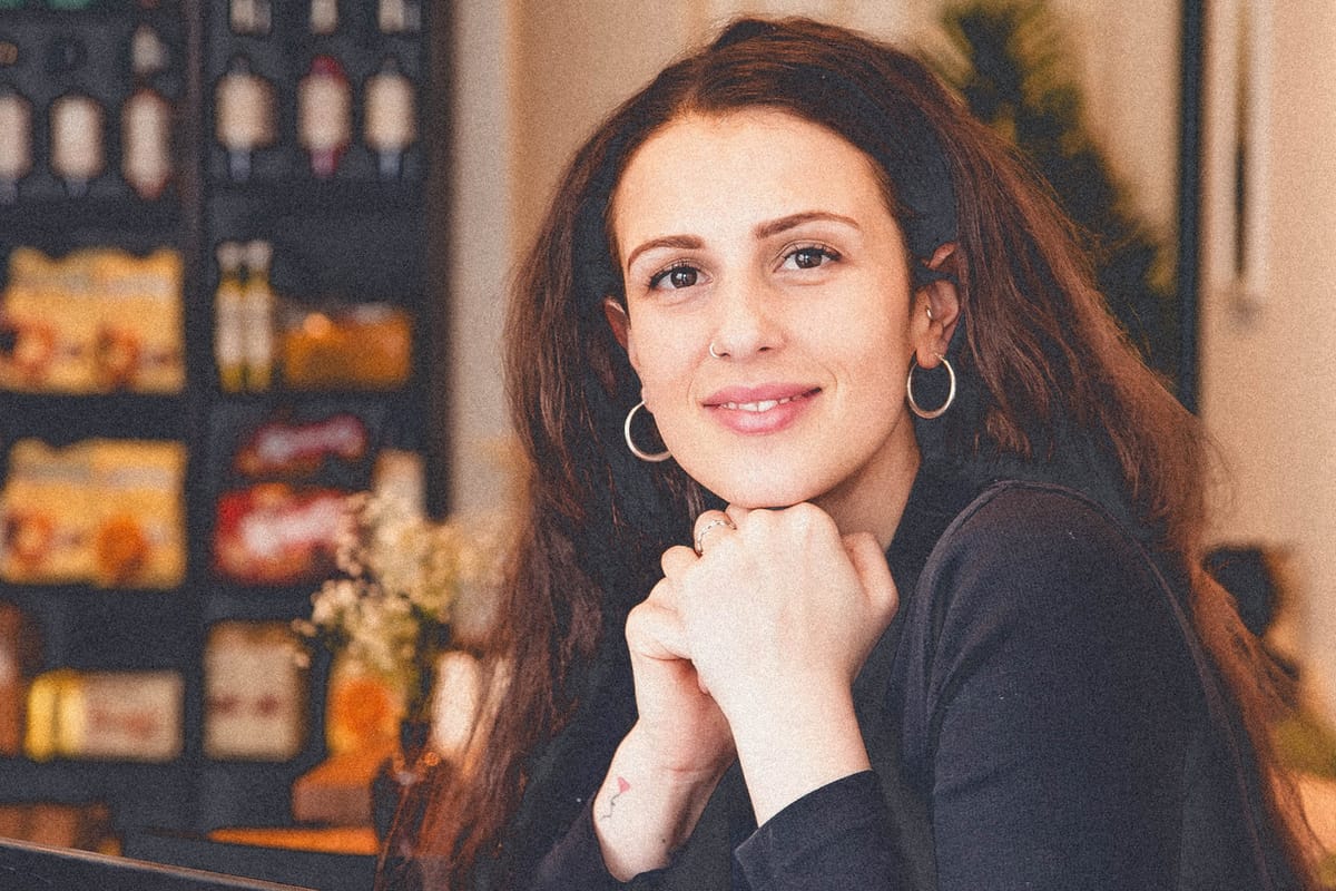 Portrait shot of Ornella Cancila smiling in her restaurant with packaged groceries on display in the background