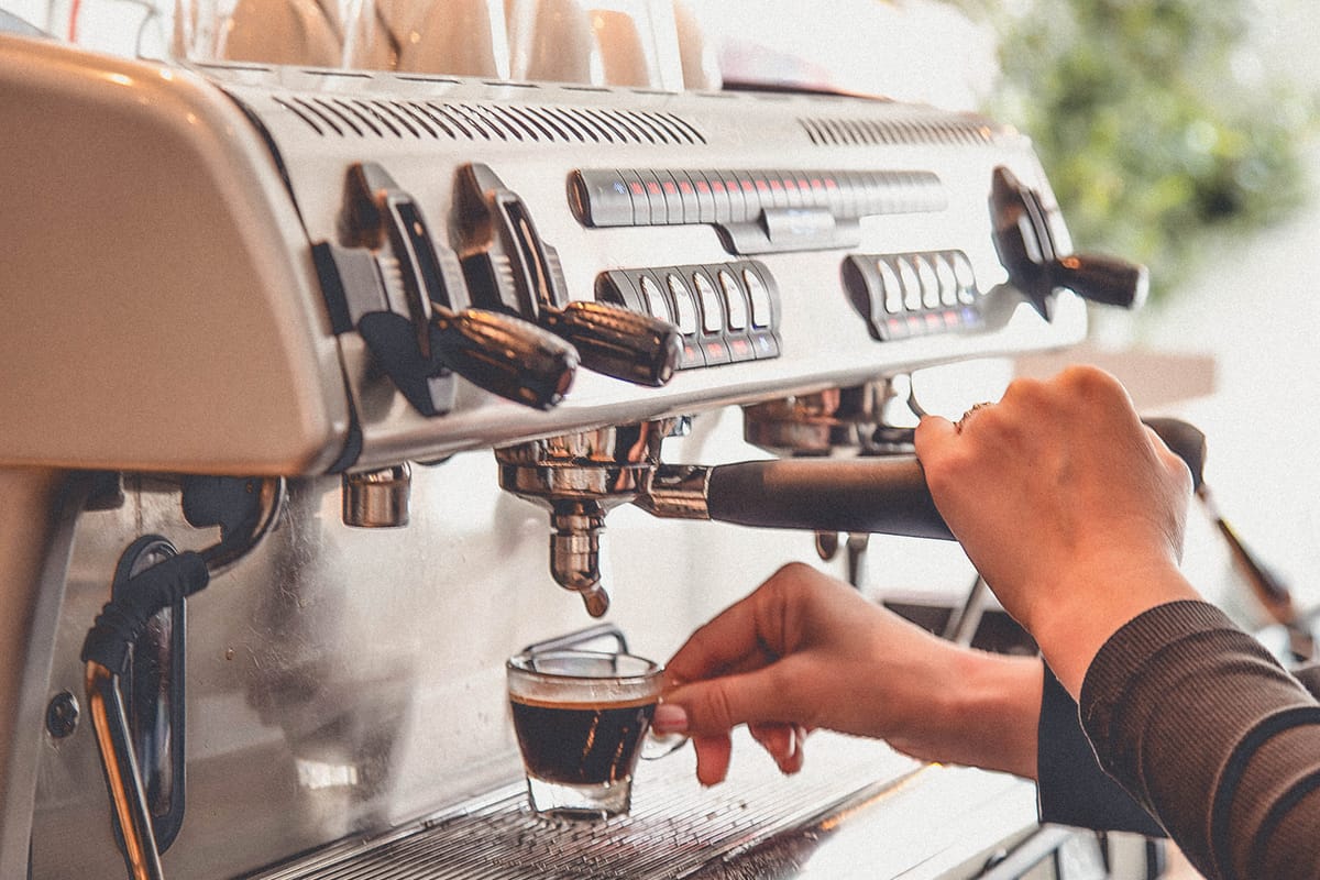 Close-up of Ornella Cancila using a commercial coffee machine to pour an espresso into a glass cup