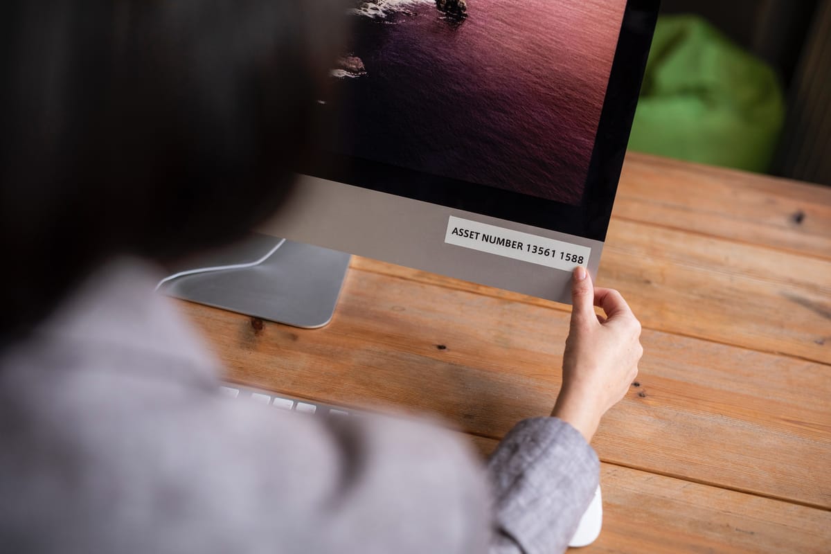 A lady applying a black on white laminated asset number tag to an all-in-one desktop computer