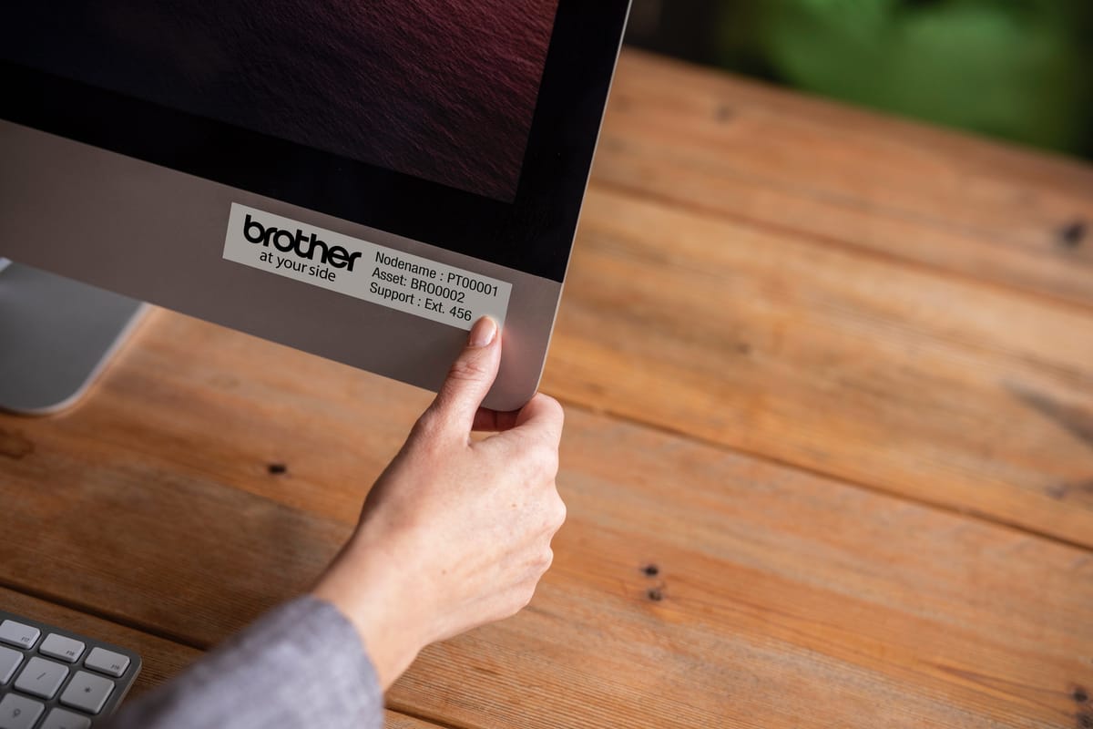 A lady applying a black on white laminated asset tag to an all-in-one desktop computer