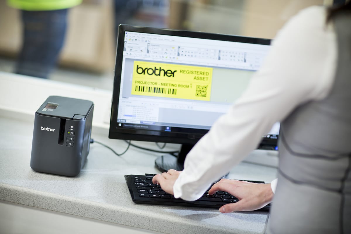 A lady using P-touch editor software to print a black on yellow QR code asset tab to a Brother label printer in a warehouse environment