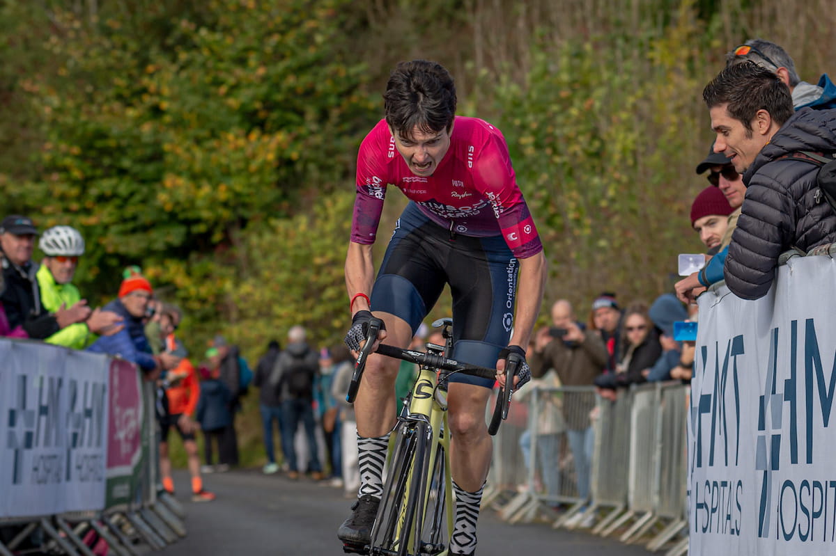 Female racing cyclist, red jersey, blue shorts, yellow bike, riding towards camera