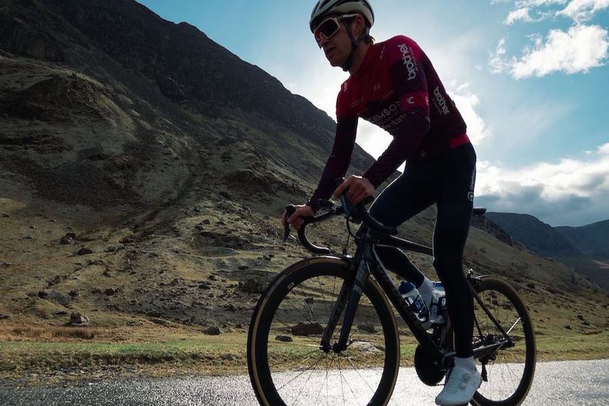 Cyclist Joey Walker riding along a country road with a mountain and blue sky in the background