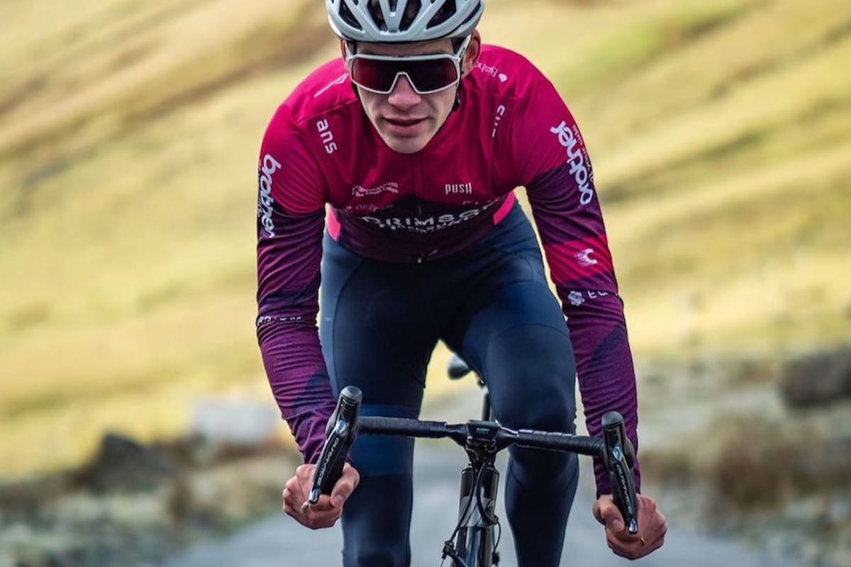 Cyclist Joey Walker leaning over his handlebars as he rides uphill with greenery in the background